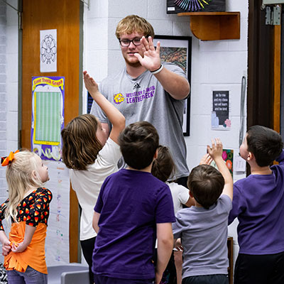 a college student high-fiving a group of excited children