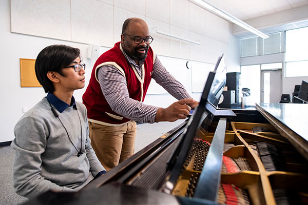 a student sitting at a piano with a teacher showing them something on the music