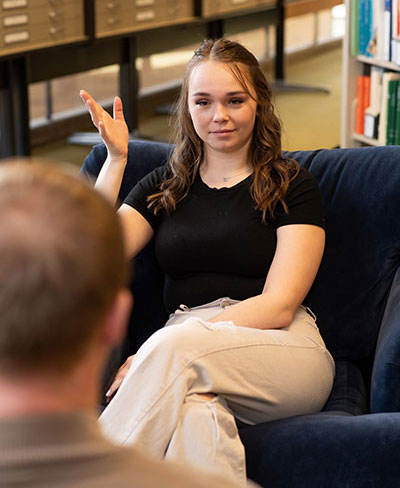 a student sitting on a couch talking to another student