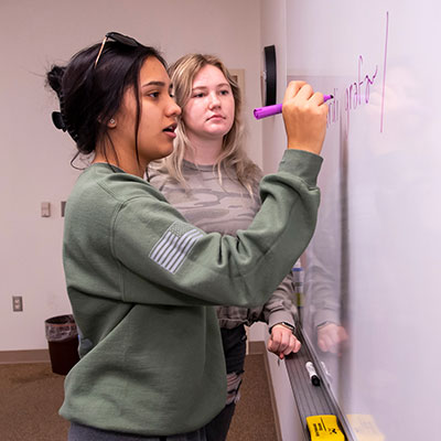 two students writing on a whiteboard