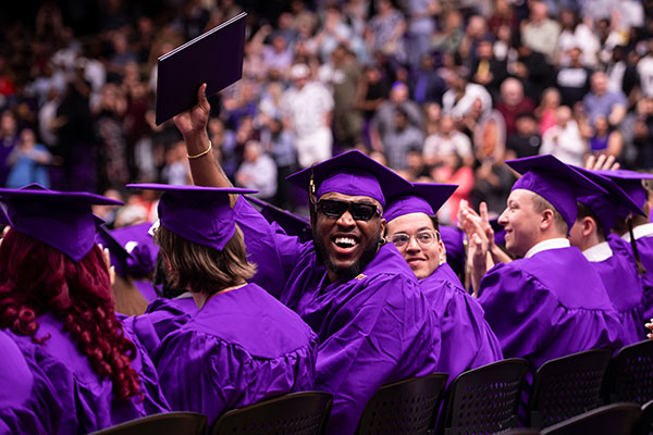 group of students at commencement with one turning around to wave