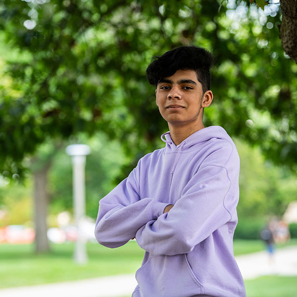 young man outside, facing the camera, arms crossed, confident look