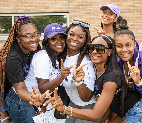 a group of young women wearing purple WIU gear and making W signs with their hands