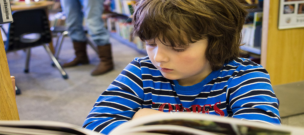 boy reading from book in library