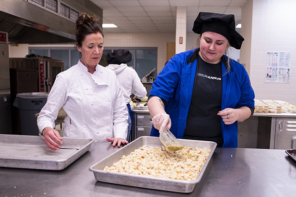 instructor watching a student pour liquid on food in a pan