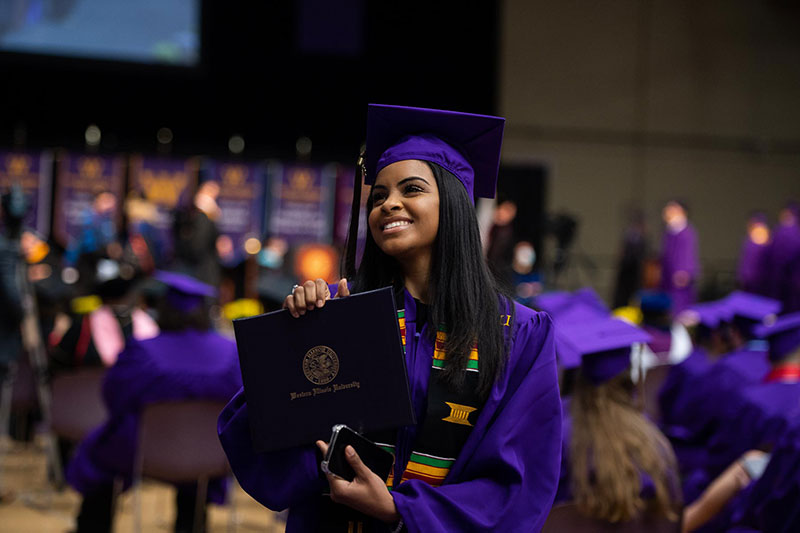 student in graduation robe walking back to seat with diploma cover