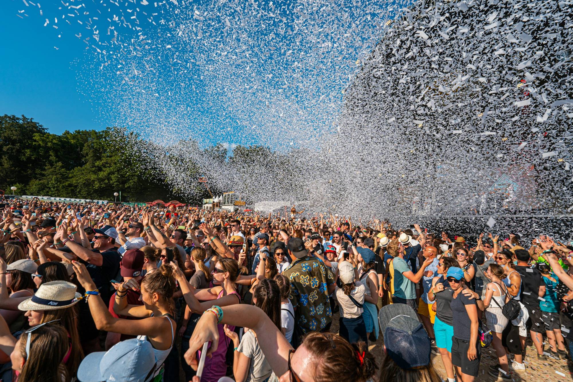 People raising their hands beneath a shower of confetti at an outdoor celebration.